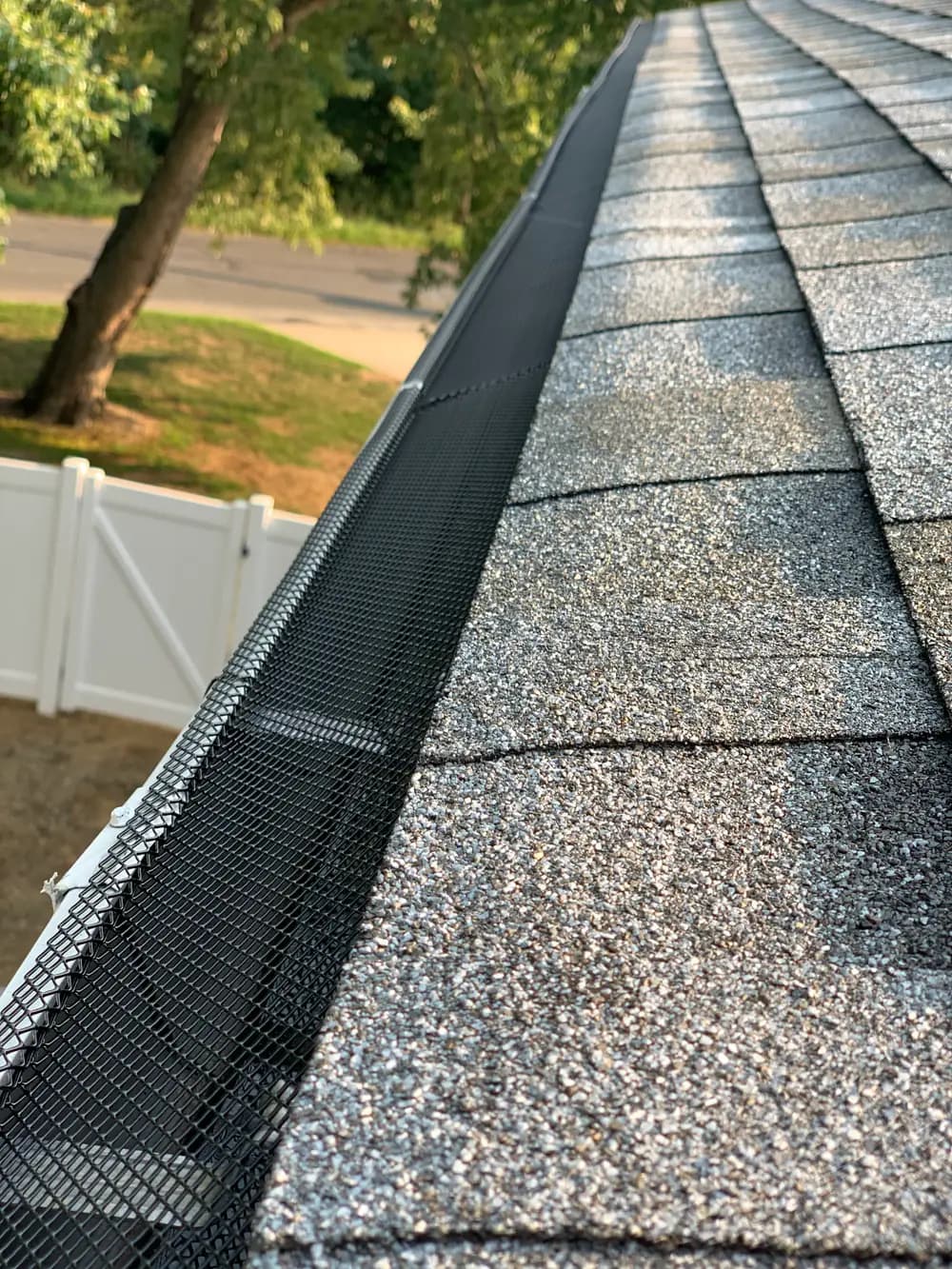 A long run of black mesh gutter guard along the edge of a shingle roof, seen from above